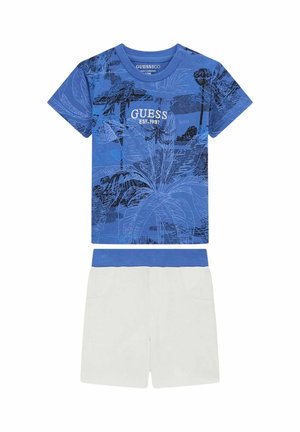 Camicia azzurra a maniche corte per bambino con stampa tropicale e scritta "GUESS EST. 1981" abbinata a pantaloncini bianchi con vita elastica blu.
