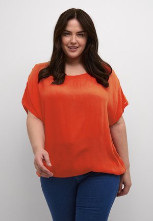 Bright orange, short-sleeve top with a loose fit and a smooth, slightly textured fabric. Paired with blue denim jeans.