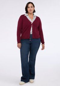 Burgundský svetřík s vlnkovaným lemem a zlatým zapínáním na knoflík přes světle šedou blůzu, doplněný tmavými zvonovými džínami a bílými teniskami.