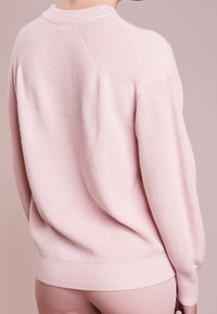 Jasnoróżowy sweter z dzianiny o ribbowym wzorze, z raglanowymi rękawami i okrągłym dekoltem, w luźnym fasonie i z ribbowym wykończeniem.