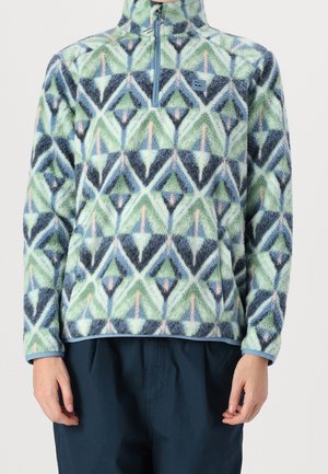 Sudadera de forro polar de manga larga con estampado geométrico verde, azul, negro y rosa, medio cierre delantero y bolsillo canguro, usada con pantalones oscuros.