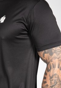 Black short-sleeve t-shirt made from smooth fabric, featuring a small white logo on the chest and a fitted design around the shoulders.