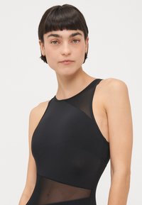 Schwarzes Sporttop mit Netzpaneelen, hohem Halsausschnitt und ärmellosem Design. Weicher Stoff mit körpernahem Schnitt und minimalen Nähdetails.