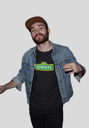 Jeansowa kurtka w jasnoniebieskim odcieniu na czarnym t-shircie z zielonym i żółtym napisem "GOING NOWHERE". Model pozuje w sposób swobodny.