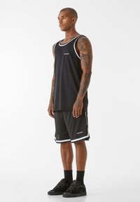 Melns sporta topiņš un šorti ar baltām akcentām, kas rotāti ar logo. Audums izskatās viegls un gluds, piemērots sporta aktivitātēm.