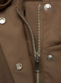 Bruine stof met een zichtbare metalen rits en drukknoopdetails. De textuur lijkt glad; het ontwerp is functioneel met strakke lijnen.