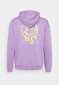 Lila huvtröja med en gul grafisk design och text på baksidan. Den har en dragsko i huvan och ribbade manschetter och nederkant. Mjukt tyg.