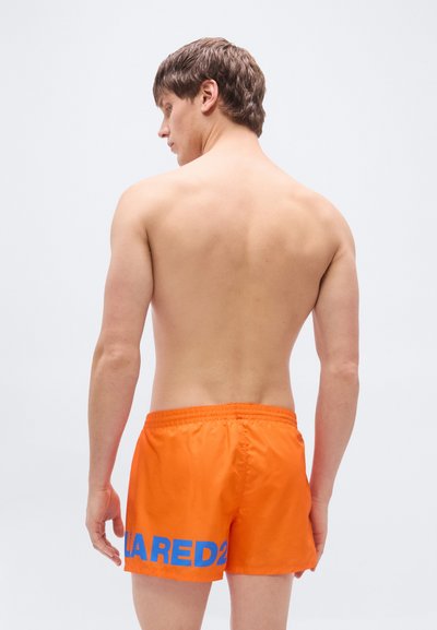 Πορτοκαλί μαγιό με ελαστική μέση, που διαθέτει μπλε λογότυπο "D squared" στην αριστερή πλευρά. Λείο, ελαφρύ ύφασμα.