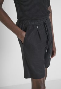 Pantaloni corti neri in tessuto con vita elastica, tasche laterali e cordoncino. Il materiale appare liscio con una leggera lucentezza.