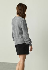 Pull en maille gris avec une finition texturée et un ourlet côtelé, associé à une jupe en suède noire, vu de dos.