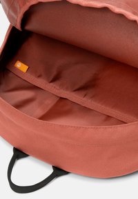 Interior de mochila de color óxido con una textura de tela suave, que presenta un solo compartimento y asas de tela negra.