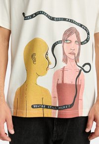 White t-shirt featuring a graphic illustration of a yellow figure and a pink figure, with text in black ribbon across the design.