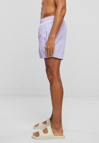 Pantaloni de înot violete deschise cu talie elastică și design cu frunze albastre. Purtați cu sandale slide de culoare albă murdară, evidențiind o potrivire relaxată și textură.