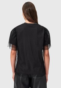 Top nero con tessuto trasparente a pois, maniche a sbuffo, scollatura rotonda semplice e vestibilità rilassata. Il design testurizzato aggiunge interesse visivo.
