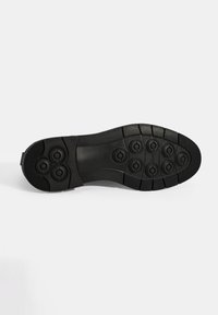 Semelle de chaussure en caoutchouc noir avec un design texturé et des motifs de grip circulaires. Présente des rainures définies et une section centrale lisse.