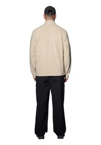 Beige fleecejacka, hög krage, bakvy. Har texten "ATW" präglad i tyget. Kombination med svarta cargobyxor.