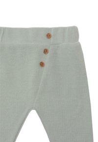 Helle grüne Leggings aus strukturiertem Stoff mit hoher Taille, ausgestattet mit drei braunen Knöpfen an der Seite als Detail.