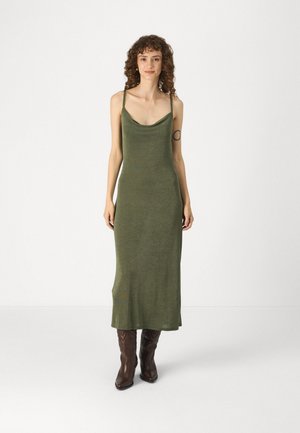 Olive green, sleeveless maxi dress with a cowl neckline, made of soft fabric; paired with brown cowboy boots. Smooth texture and fitted silhouette.