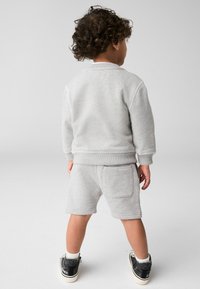 Sivý dvojdielny outfit pre deti, ktorý obsahuje mikinu a šortky. Mäkkučká textúra, rebrované manžety a zadná vrecko na šortkách.