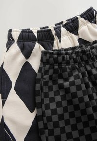 Due pantaloni con elastico in vita: uno presenta un grande motivo astratto blu navy e crema, l'altro ha un piccolo design a scacchi nero e grigio.