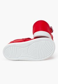 Scarpe in pelle rossa con punta rotonda e suola in gomma bianca. Tra le caratteristiche ci sono una chiusura con fibbia e una suola testurizzata per la presa.