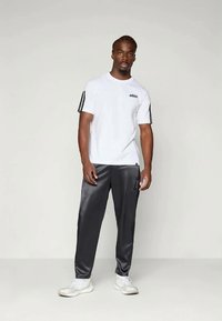 Hvit treningst-skjorte med svart logo og tre svarte striper på ermene, kombinert med glatte svarte treningbukser og hvite joggesko.