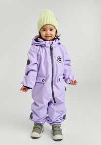 Fioletowy wodoodporny kombinezon narciarski z kapturem, elastycznymi mankietami, czarnymi akcentami, zamkiem z przodu i kieszeniami, w zestawie z jasnoszarym dzianinowym czapkiem i szarymi butami.