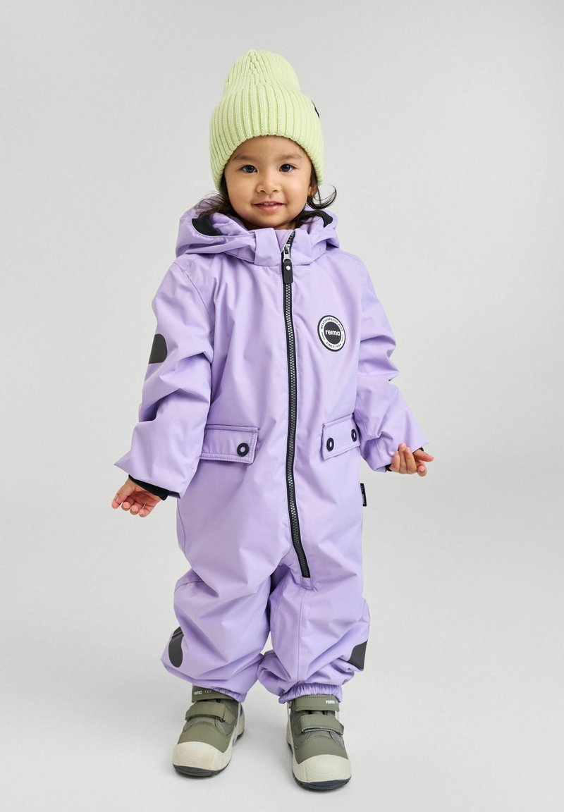 Fioletowy wodoodporny kombinezon narciarski z kapturem, elastycznymi mankietami, czarnymi akcentami, zamkiem z przodu i kieszeniami, w zestawie z jasnoszarym dzianinowym czapkiem i szarymi butami.