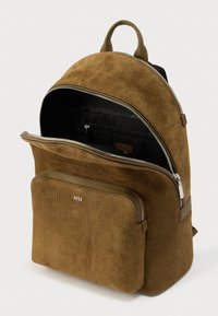 Καφέ σακίδιο πλάτης από σουέντ με υφή, διαθέτει εμπρόσθια τσέπη με φερμουάρ και δύο μεταλλικά φερμουάρ. Το εσωτερικό είναι μαύρο με επιπλέον χώρο αποθήκευσης.