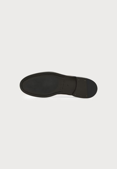 Semelle de chaussure habillée en cuir noir, affichant une finition lisse avec un bord cousu et un talon renforcé avec des clous métalliques.