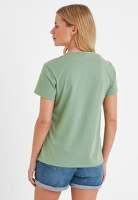 Green cotton t-shirt with short sleeves and a crew neck. The back shows a smooth texture and a slightly rounded hem, paired with denim shorts.