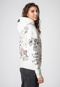 White hoodie with front pocket, featuring colorful graphic designs, including flowers and text. Soft fabric, relaxed fit, and ribbed cuffs.