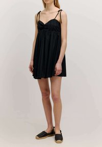Zwarte geplooide jurk met verstelbare strappy bandjes en een sweetheart halslijn. Vloeiende silhouet, gemaakt van lichtgewicht stof. Gecombineerd met zwarte espadrilles.