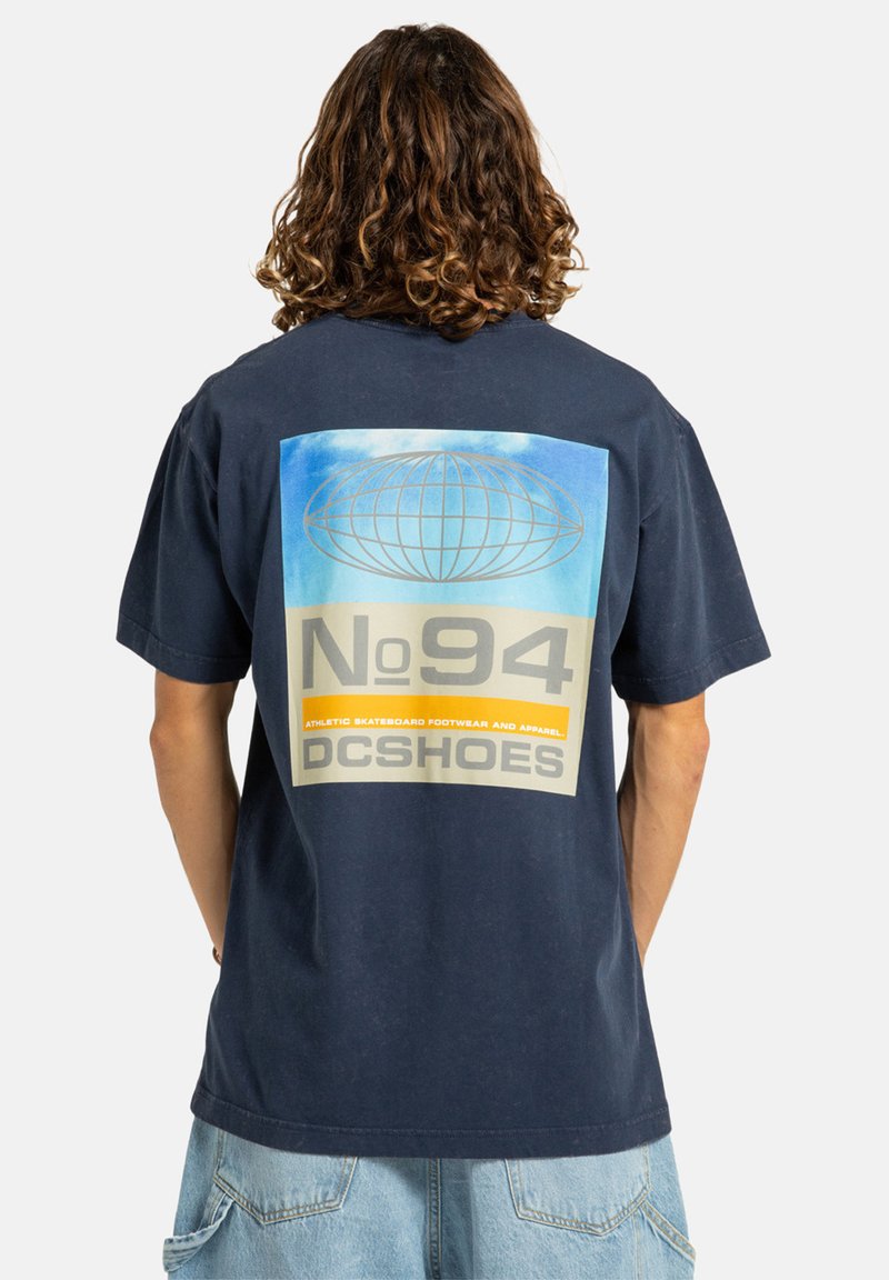Námořnické bavlněné tričko s velkým potiskem na zádech, který zobrazuje globus, text "No94" a "DCSHOES" v žlutých a šedých akcentů.