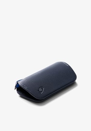 Portefeuille en cuir bleu marine avec une texture lisse, des bords arrondis et une fermeture à rabat. Présente un logo subtilement embossé sur le devant.