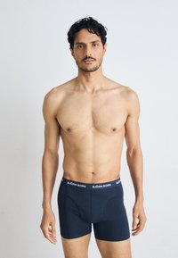 Fekete pamut boxer alsónadrág, szoros szabással és fehér "BJÖRN BORG" logóval a deréknál, modell felső nélkül, semleges háttérrel.