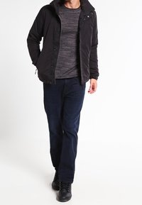 Czarna kurtka z kapturem, szara teksturowana koszula i ciemnoniebieskie spodnie; strój uzupełniają czarne buty. Casualowy design, minimalistyczne detale.