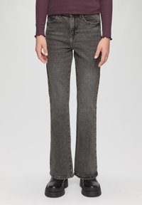 Zwarte flared jeans met een vervaagde textuur, een vijf-pocket ontwerp en subtiele stikdetails, gecombineerd met zwarte boots met dikke zolen.