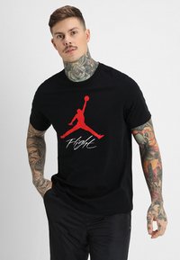 Svart bomull T-skjorte med rødt Jordan-logo og "Flight"-tekst, med korte ermer og klassisk passform.