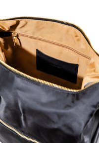 Interno di una borsa in tessuto nero con una rivestimento liscio color nocciola, dotata di una tasca con zip e un'etichetta con superficie testurizzata. Chiusura con zip dorata.