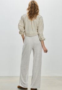 Chemise à rayures claires à manches longues en beige doux, associée à un pantalon ample gris chiné. Le tissu semble texturé et décontracté.