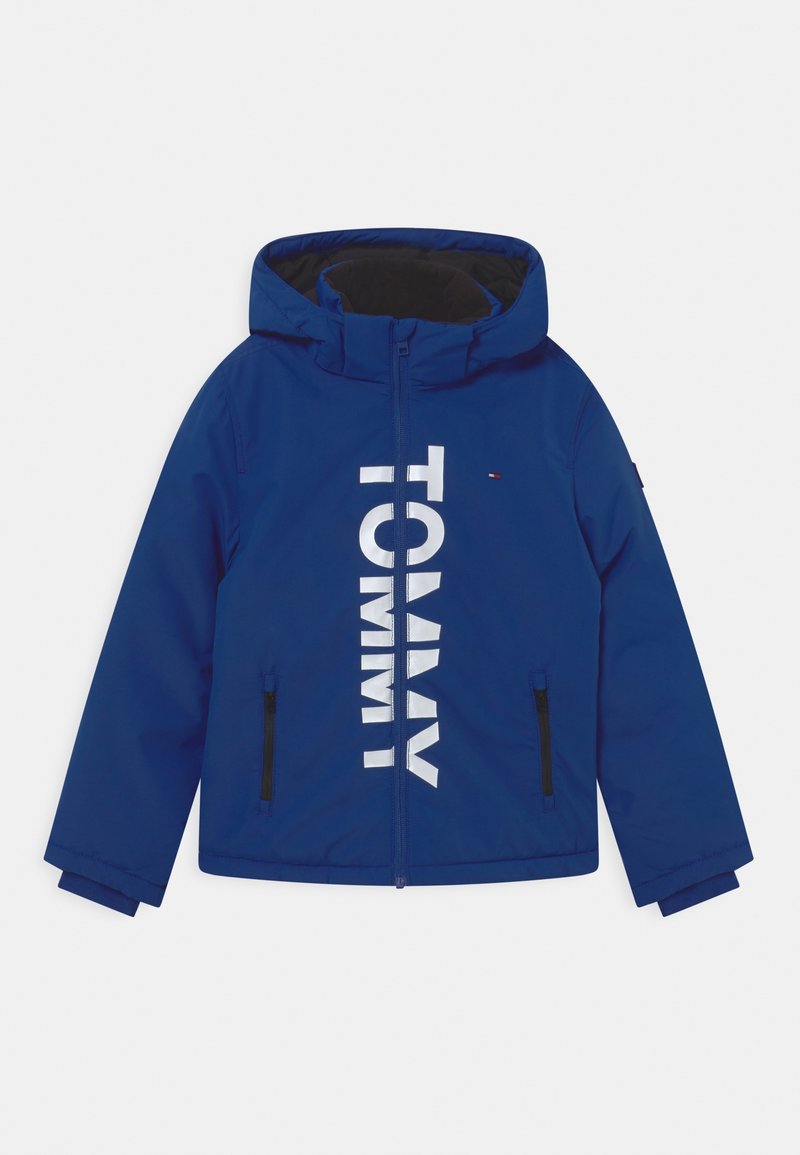 Blauwe waterdichte jas met capuchon, ritssluiting aan de voorkant en grote witte "TOMMY" tekst. Inclusief zwarte ritszakken aan de zijkanten.