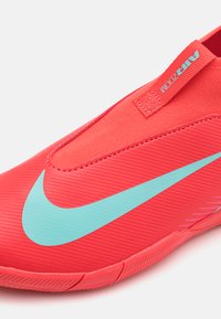 Piros sportcipő sima textúrával, nagyméretű türkizsínű pipa emblémával és slip-on dizájnnal, a "AIR ZOOM" címkével.