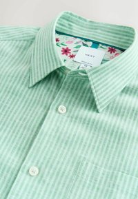 Chemise rayée verte et blanche avec un col boutonné, présentant une doublure à motif floral et une poche poitrine unique.