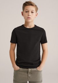 Juoda trumpomis rankovėmis medvilninė marškinėliai su klasikine apvaliomis kaklo linija, dėvimi su šviesiai chaki spalvos kelnėmis. Paprastas dizainas, be matomų raštų ar logotipų.