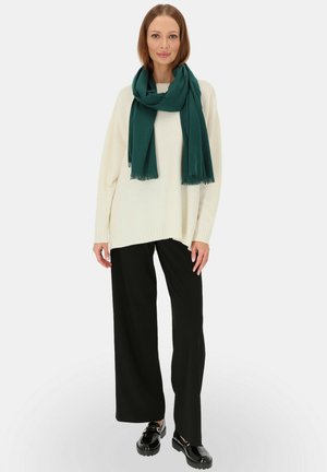 Przesadny kremowy sweter, ciemne szerokie spodnie i ciemnozielony szalik z frędzlami. Czarne lakierowane mokasyny dopełniają całość.