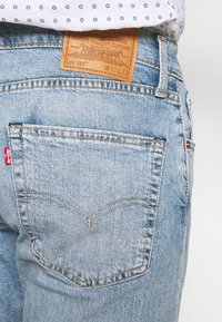 Jeans de denim azul claro con una parche de cuero que presenta la etiqueta "Levi's 502". El bolsillo trasero tiene costuras en contraste y una etiqueta roja.