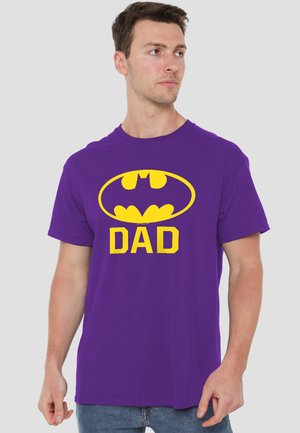 Man wearing purple t-shirt with yellow Batman logo and word "DAD" printed on front, looking to his right.