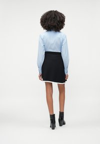 Svetlomodrá košeľa s gombíkmi v kombinácii s čiernou sukňou s bielym lemovaním. Čierne členkové topánky dokresľujú outfit. Hladká textúra, upravený strih.