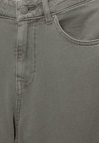 Gros plan sur un jean en denim gris montrant la taille, le bouton, la boucle de ceinture, la poche avant et les détails des rivets métalliques.